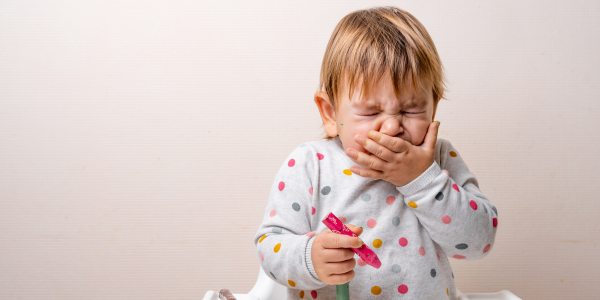 Malé dítě s rýmou kýchá a zakrývá si ústa rukou