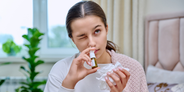 Žena s rýmou si do nosu aplikuje nosní sprej